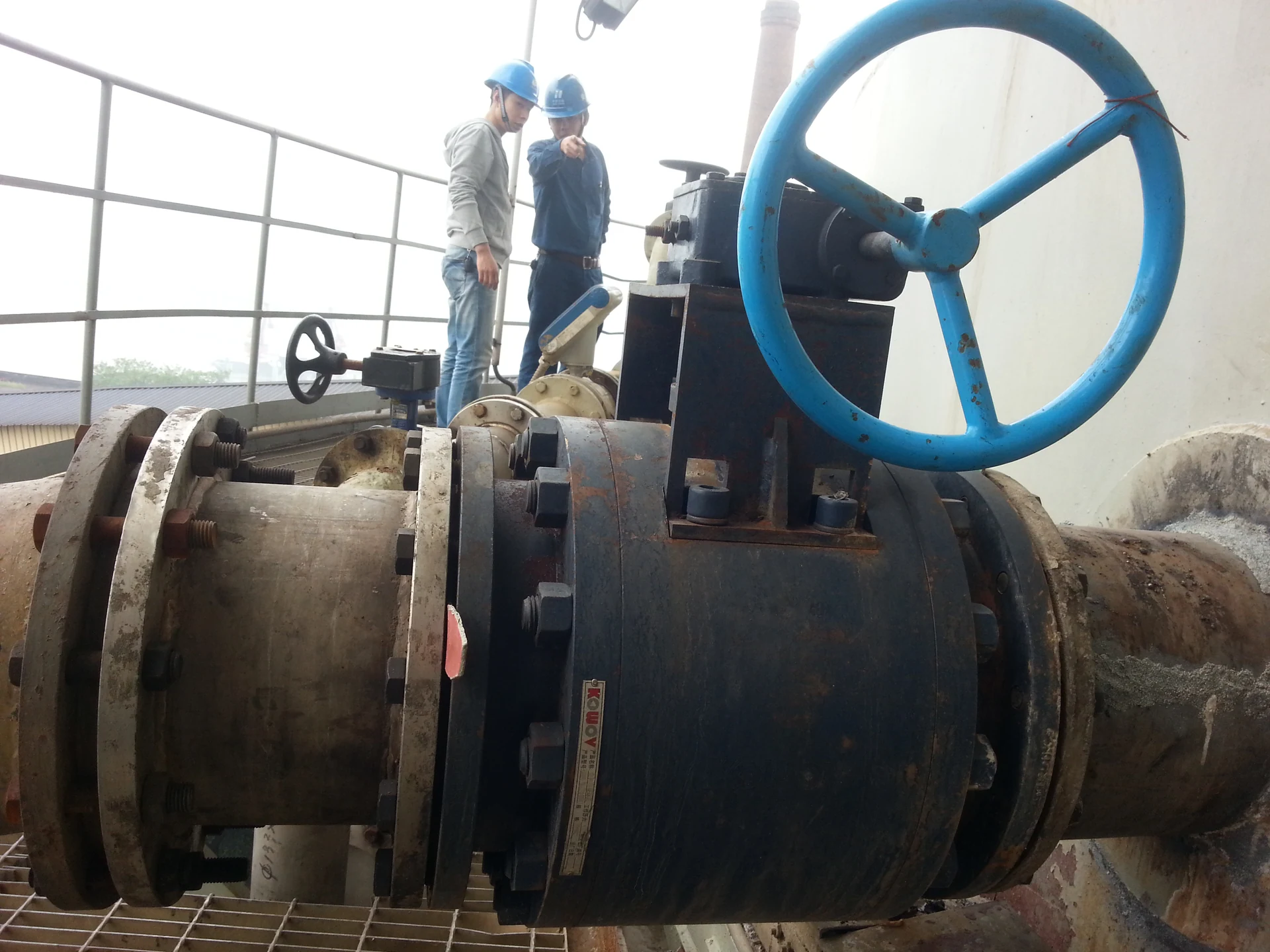Two engineers beside an installed valve with a large blue handwheel